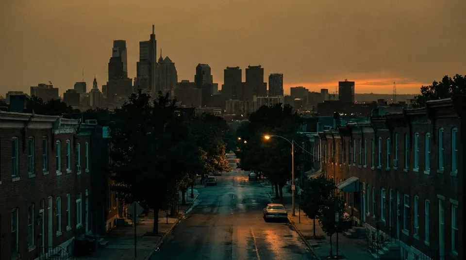 City skyline at dusk under an amber sky with a distant glow on the horizon